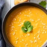 An overhead shot of a bowl of creamy sweet potato coconut soup, served with some chunky bread.
