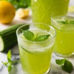 An image showing two glasses of Cucumber Mint Lemonade, and a pitcher half filled with it.