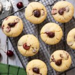 An overhead shot of a bunch of freshly baked cherry muffins cooling on a rack, with powdered sugar on the side, and some fresh cherries.
