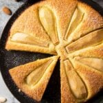 An overhead shot of fresh pear cake, with a slice ready for serving, sprinkled with powdered sugar.