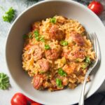 An overhead shot of Italian Sausage on a plate, with fresh cherry tomatoes and parsley on the background.