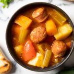 An overhead shot of a bowl of Italian sausage stew with vegetables with some chunky bread on the side.