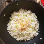 An overhead shot of a pan of just-cooked garlic fried rice, with spring onions on top, and ready for serving.
