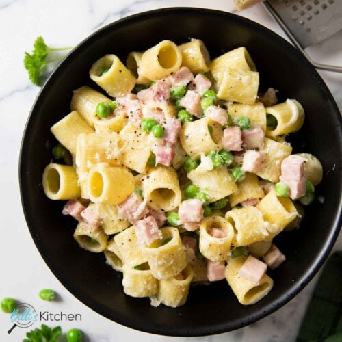 Feature image for Pasta with Ham and Peas, showing it on a plate, with grated cheese and black pepper as garnish.