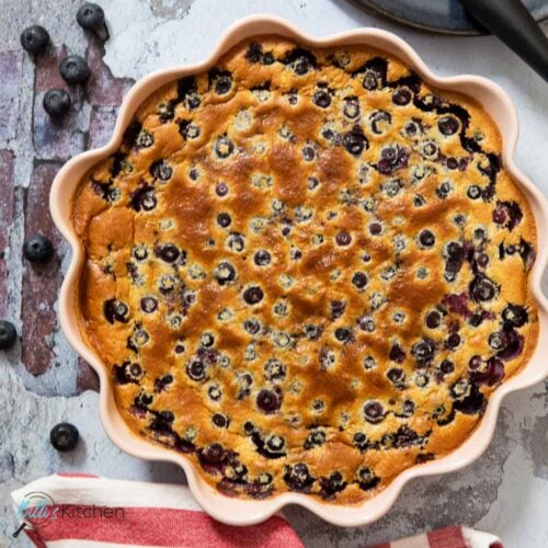 Feature image for simple blueberry clafoutis, showing one in a pie dish, ready for slicing.
