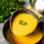 Carrot ginger soup being transferred into a serving bowl, highlighting the creaminess of the soup.