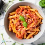Feature image for Italian sausage and peppers pasta, showing the dish on a plate, topped with grated cheese and fresh basil.