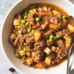An overhead shot of a plate of beef picadillo, with a bowl of white rice next to it.