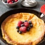 A skillet of baked pancake, ready for serving, with fresh fruits.