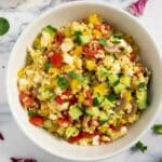 An overhead shot of Bulgur Salad with Cucumber and Tomatoes, with green-leaf vegetables around it.
