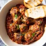 A serving of baked meatballs in sauce, with slices of bread.