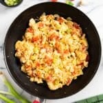 Scrambled eggs with onions and tomatoes, with chopped spring onions next to it, for serving.