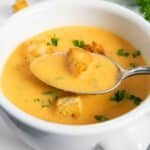A spoonful of tomato zucchini soup, with bits of croutons as garnish.