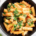 A closer shot of a serving of pasta with spinach and tomatoes, highlighting its creaminess.