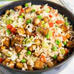 Fried rice with tofu, garnished with spring onions, served in a bowl.