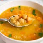 A spoonful of soup with chickpeas and sweet potatoes, highlighting the texture of the soup.