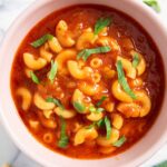 A serving of tomato and pasta soup, garnished with chopped parsley leaves.