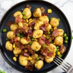 A plate of gnocchi, bacon and peas, lightly fried in a pan.