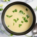 A bowl of creamy potato celery soup, garnished with fresh parsley.