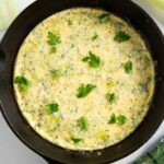 A skillet of frittata with leeks, garnished with fresh parsley, ready for serving.