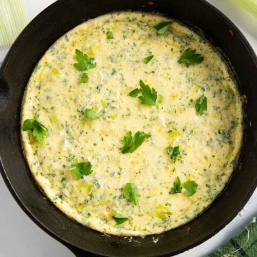 A skillet of frittata with leeks, garnished with fresh parsley, ready for serving.
