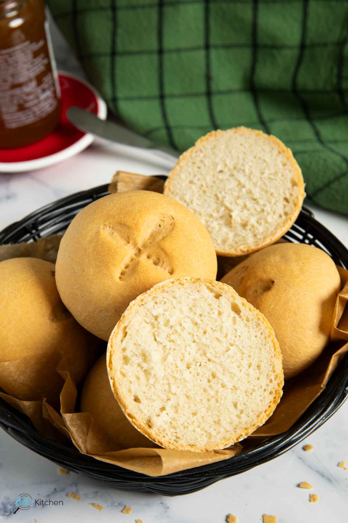 Homemade buns with yogurt served on a basket with marmalade and butter knife in the background.