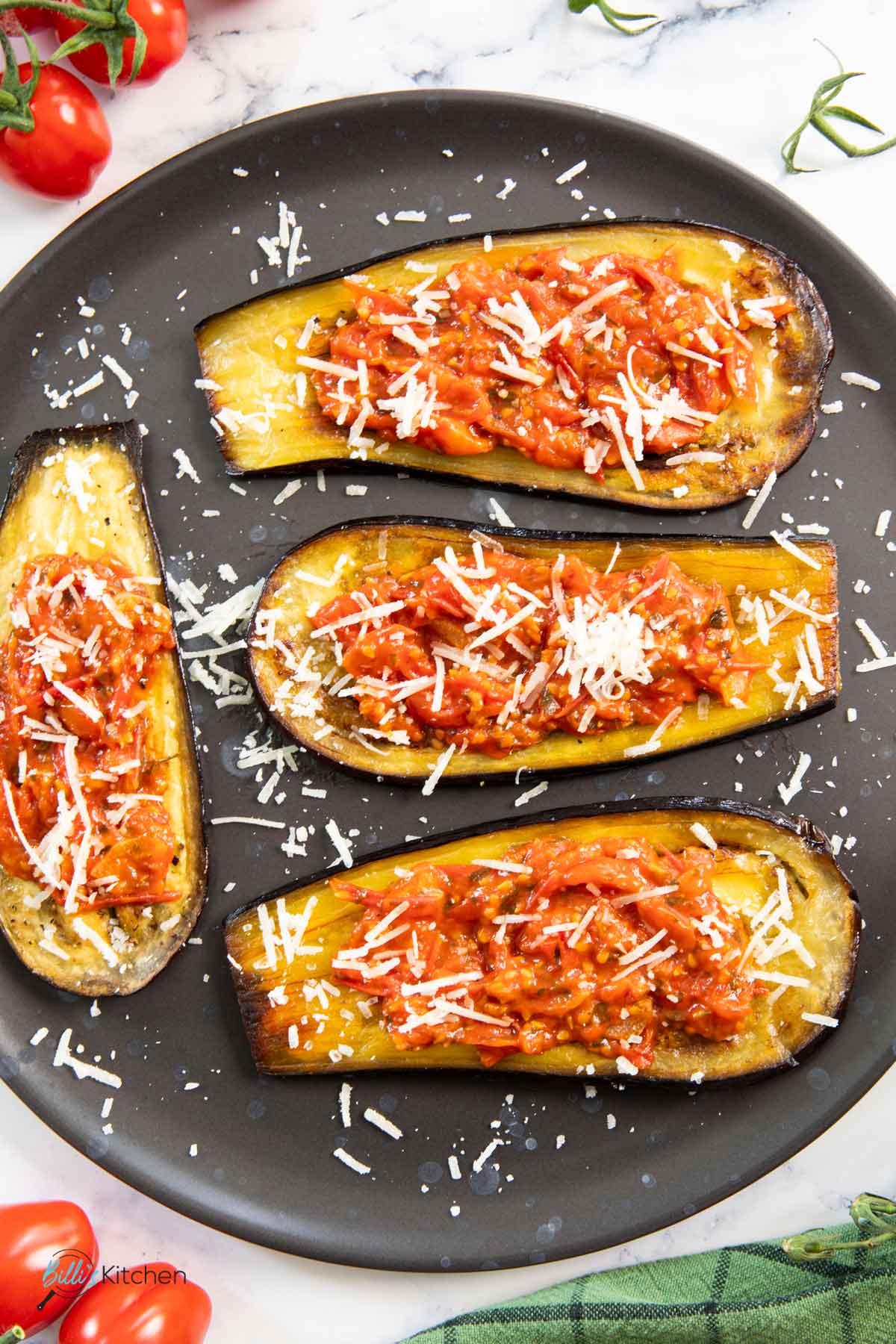 A plate of eggplants roasted in the oven, and topped with tomatoes and cheese.