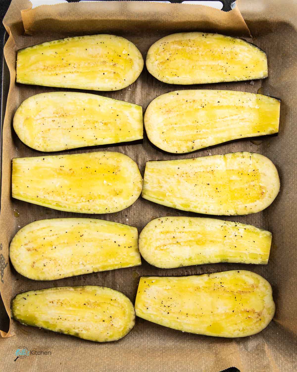 Brushing the eggplant slices with olive oil and seasoning with salt and pepper, before roasting.