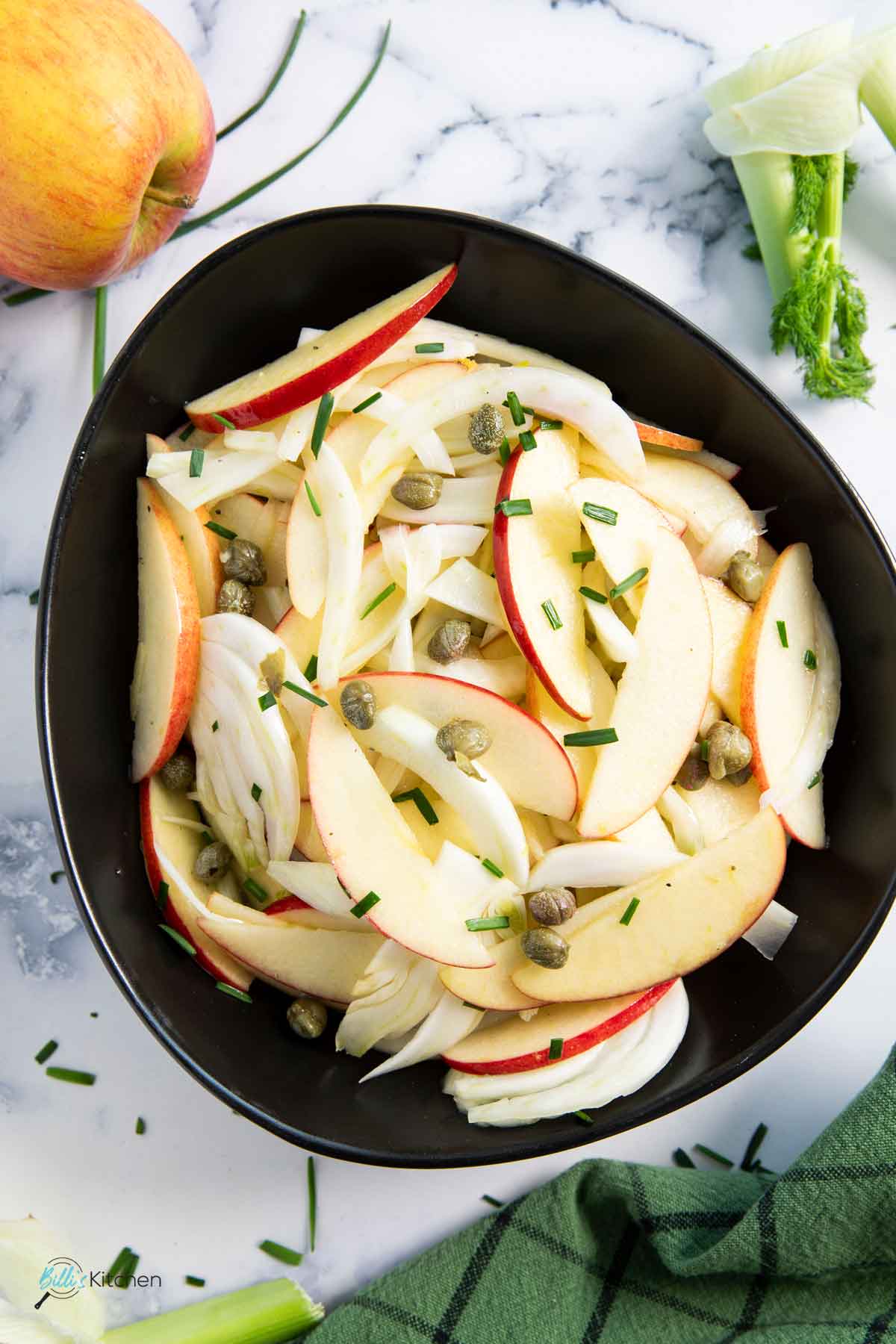 A bowl of fresh apple and thin fennel slices with capers and olive oil for salad dressing.