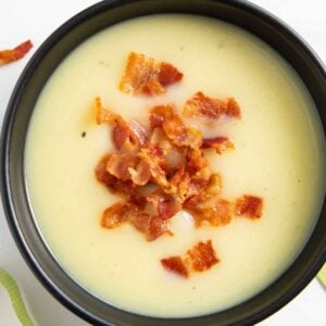 A bowl of potato and leek soup, garnished with crispy bits of bacon.