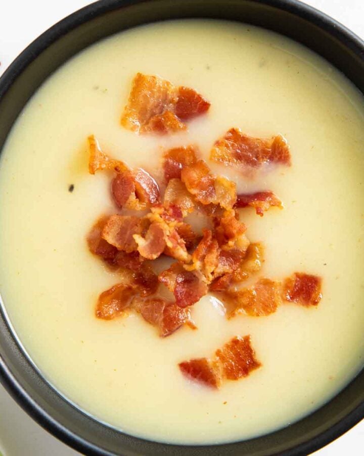 A bowl of potato and leek soup, garnished with crispy bits of bacon.