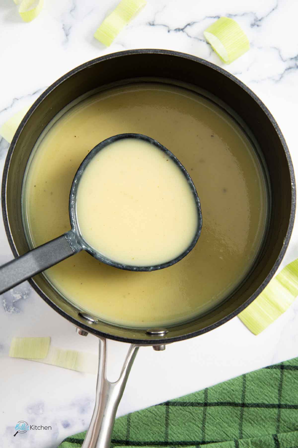 A ladle of velvety soup made of pureed leeks and potatoes, ready for transferring into a bowl.