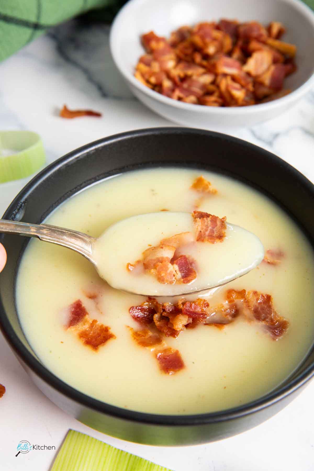 A spoonful of leek and potato soup, with crispy bacon on the side.