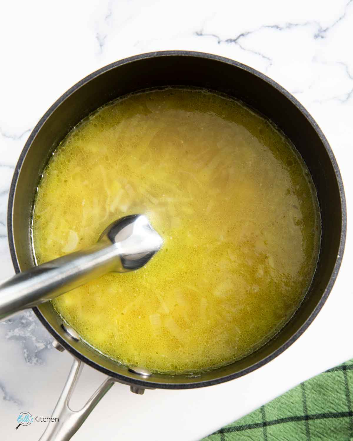 Using an immersion blender to puree the leeks and potato in the pan.