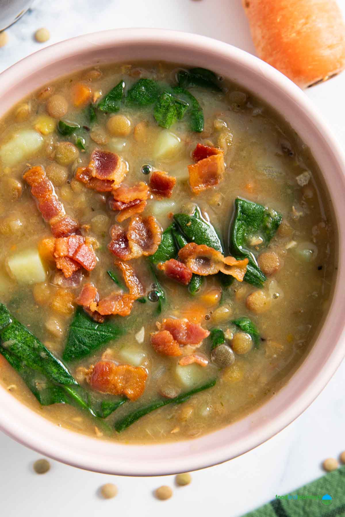A bowl of homemade soup of lentil and bacon, with spinach and potatoes, served.