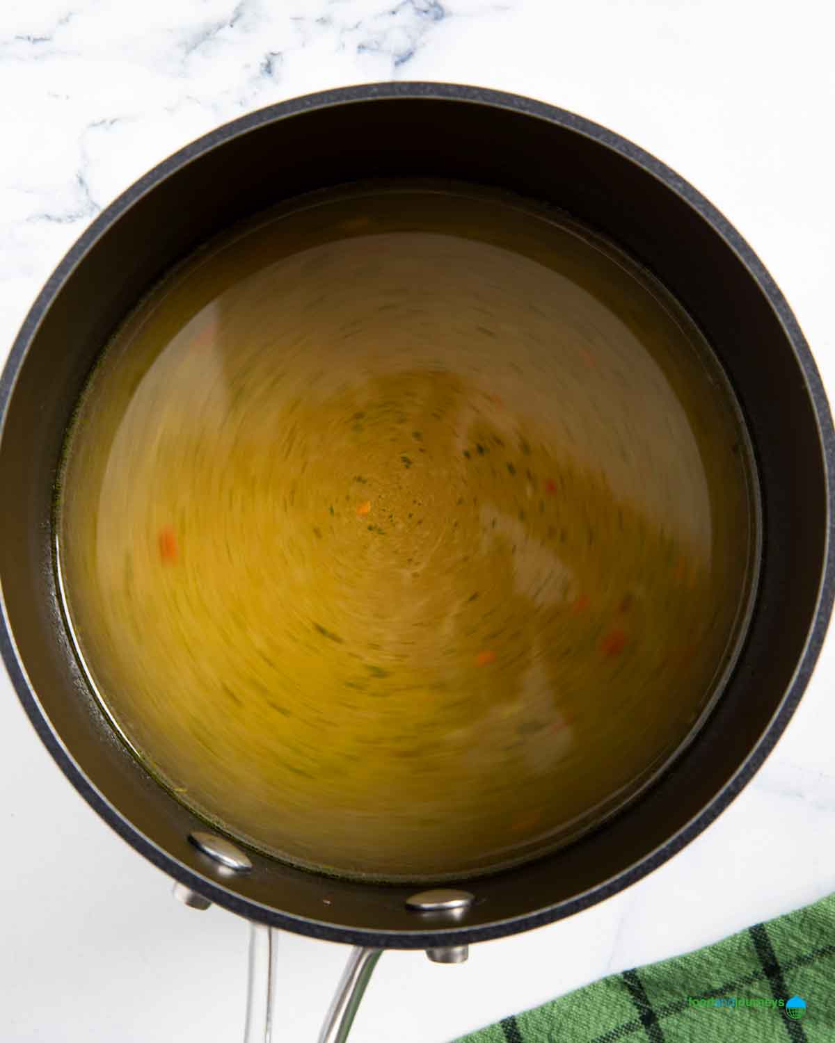 Pouring vegetable stock to use for cooking the green lentils in the soup.